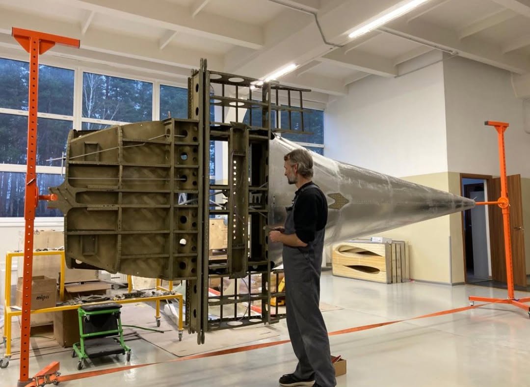 Belmont craftsman inspecting a bare aluminum fuselage assembly in the workshop jig